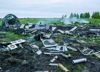 Wreckage of crashed plane scattered across field, smoke rising.