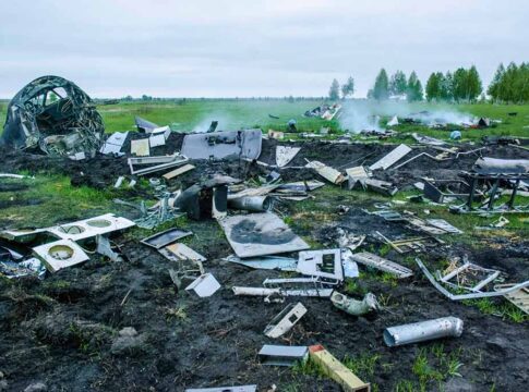 Wreckage of crashed plane scattered across field, smoke rising.