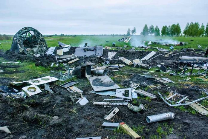 Wreckage of crashed plane scattered across field, smoke rising.