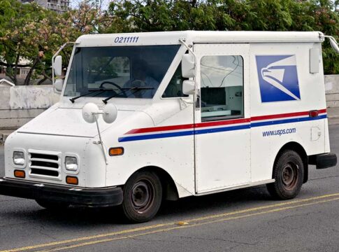 USPS delivery truck driving on urban street.