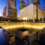 911 Memorial at night with surrounding city buildings.