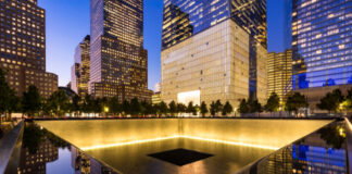 911 Memorial at night with surrounding city buildings.