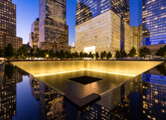 911 Memorial at night with surrounding city buildings.