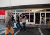 People running by a vandalized building with broken windows.