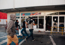 People running by a vandalized building with broken windows.