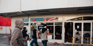 People running by a vandalized building with broken windows.