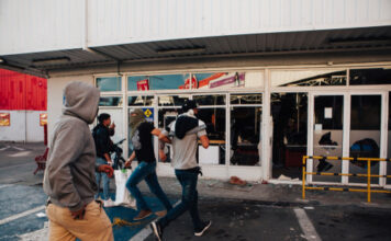 People running by a vandalized building with broken windows.