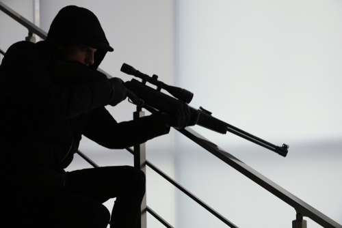 Person in dark clothing aiming a rifle indoors.