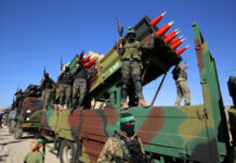 Armed soldiers on a truck with mounted missiles.