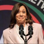 A woman in a light suit speaks at a podium.