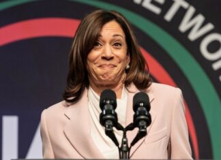 A woman in a light suit speaks at a podium.