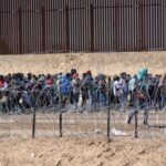 Large group of people behind barbed wire fence.