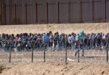 Large group of people behind barbed wire fence.