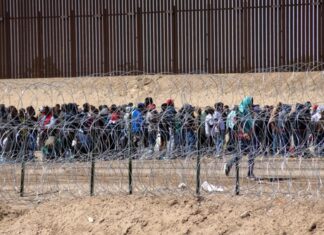 Large group of people behind barbed wire fence.