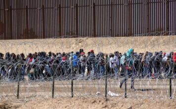 Large group of people behind barbed wire fence.