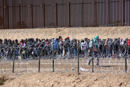 Large group of people behind barbed wire fence.