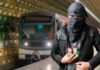 Man with cloth-covered face holding device in subway.