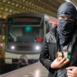 Man with cloth-covered face holding device in subway.