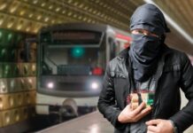 Man with cloth-covered face holding device in subway.