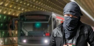 Man with cloth-covered face holding device in subway.