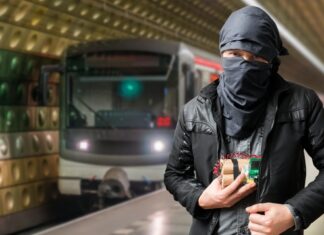 Man with cloth-covered face holding device in subway.