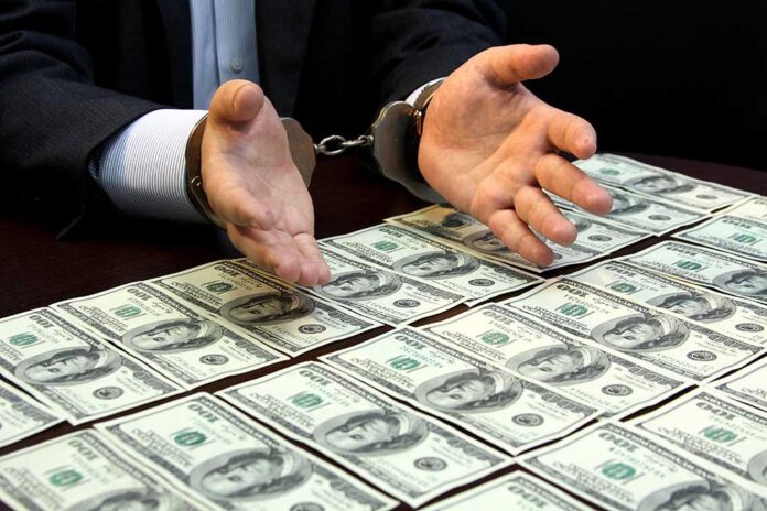 Handcuffed hands over a table of hundred-dollar bills.