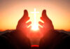 Hands reaching toward sun and cross at sunrise.