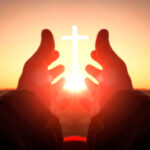 Hands reaching toward sun and cross at sunrise.