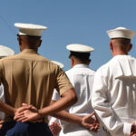 People in military uniforms standing with hands behind backs.