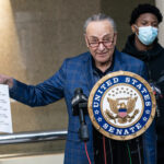 Chuck Schumer holds document at United States Senate podium.