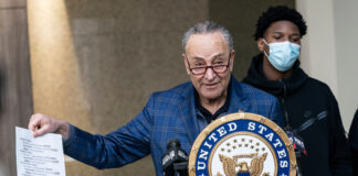 Chuck Schumer holds document at United States Senate podium.