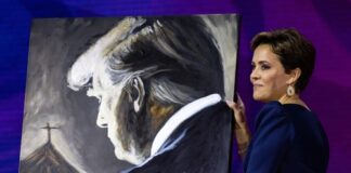 A woman holding a painting of Donald Trump.