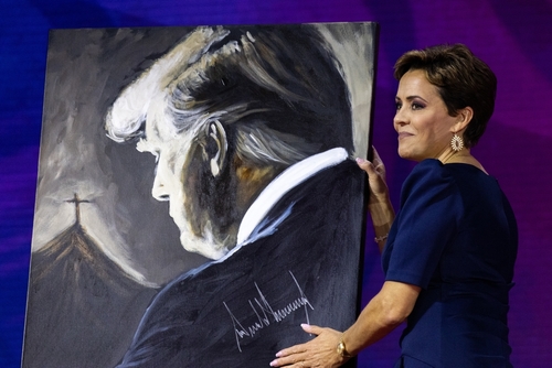 A woman holding a painting of Donald Trump.