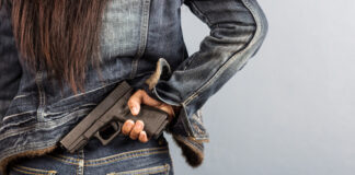 Person in denim jacket concealing handgun behind back.