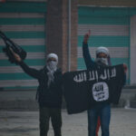 Two masked individuals with a weapon and ISIS flag.