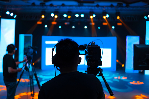 Camera operators filming a brightly lit stage.