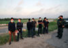 People wearing masks stand near border patrol agents outdoors.