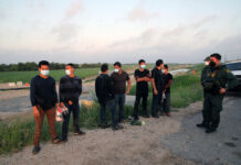 People wearing masks stand near border patrol agents outdoors.