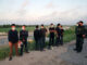 People wearing masks stand near border patrol agents outdoors.