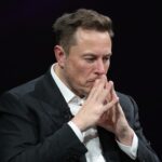 Elon Musk deep in thought, hands clasped near face.