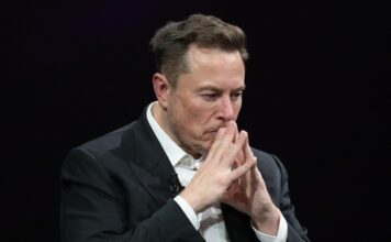 Elon Musk deep in thought, hands clasped near face.