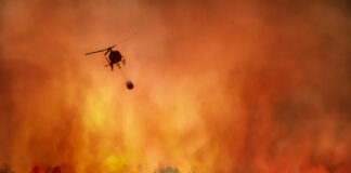 Helicopter fighting large wildfire in a forest.