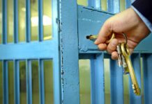 Hand unlocking a metal gate with keys.