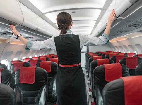 Flight attendant inspects overhead compartments in empty airplane.