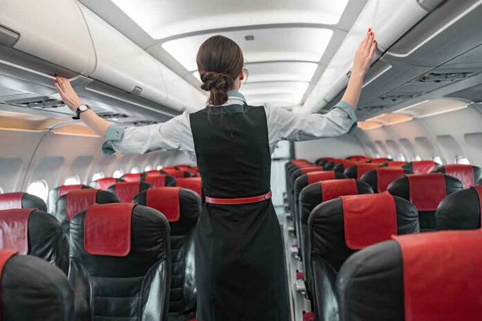 Flight attendant inspects overhead compartments in empty airplane.