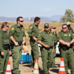 Uniformed officers standing outdoors next to traffic cones.