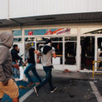 People running by a vandalized building with broken windows.