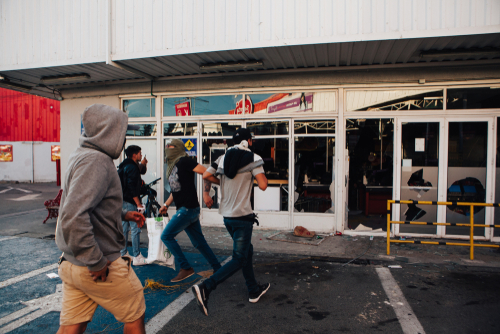 People running by a vandalized building with broken windows.