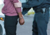 Police officer arresting a person near a vehicle.