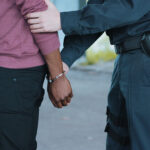 Police officer arresting a person near a vehicle.